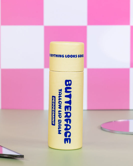 tallow butter lip balm named Butterface in a plastic-free tube against a pink tiled background